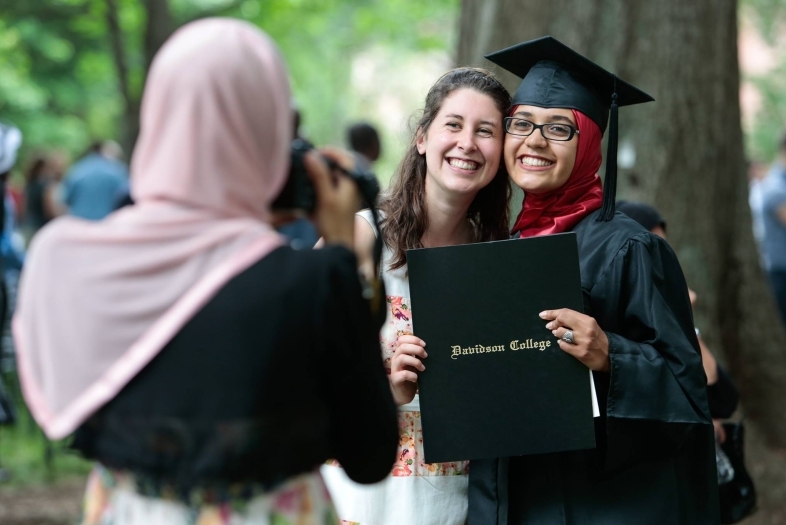 Friends hold diploma while family member takes photo of them
