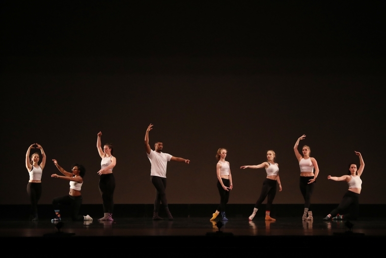 Dancers on stage take different positions in front of a black background