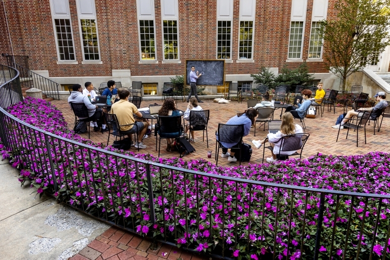 Davidson College Professor Hammurabi Mendes teaches class students outdoors with chalkboard surrounded by purple flower bushes