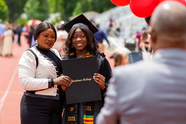 Commencement Ceremony where Graduate Holds Diploma and Hugs Family Member