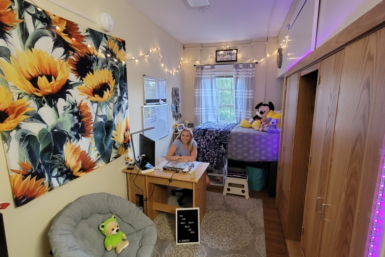 student sitting at desk in her decorated, single dorm room