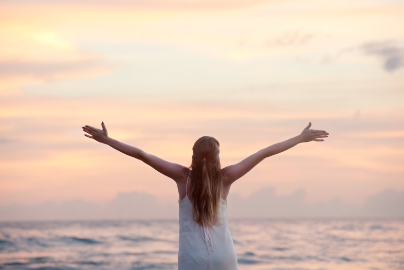 women with arms stretched out at beach stock
