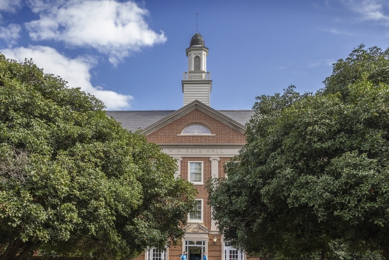 a brick building surrounded by green trees and blue skies in the background