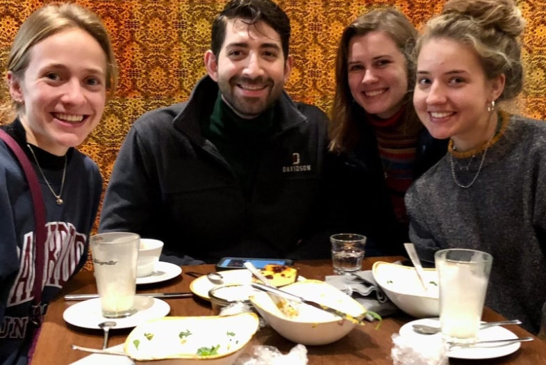 three young women and a young man smile while sitting around a restaurant table together