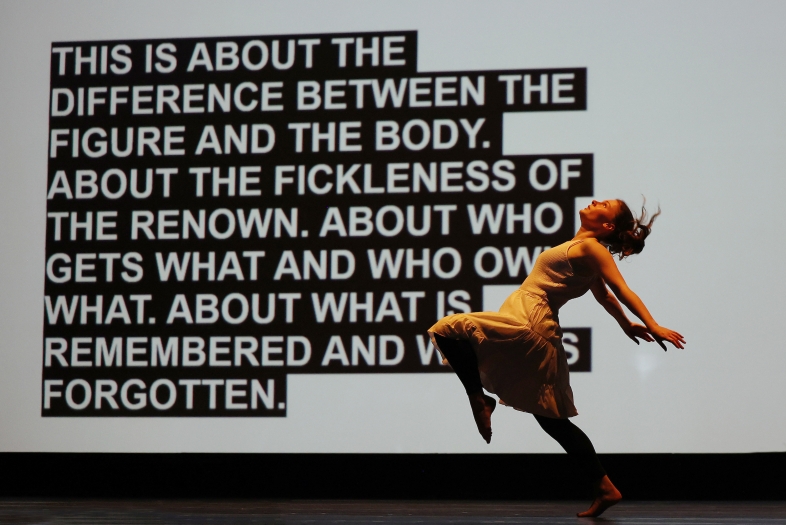 a dancer moves in front of a screen with a block of text on it