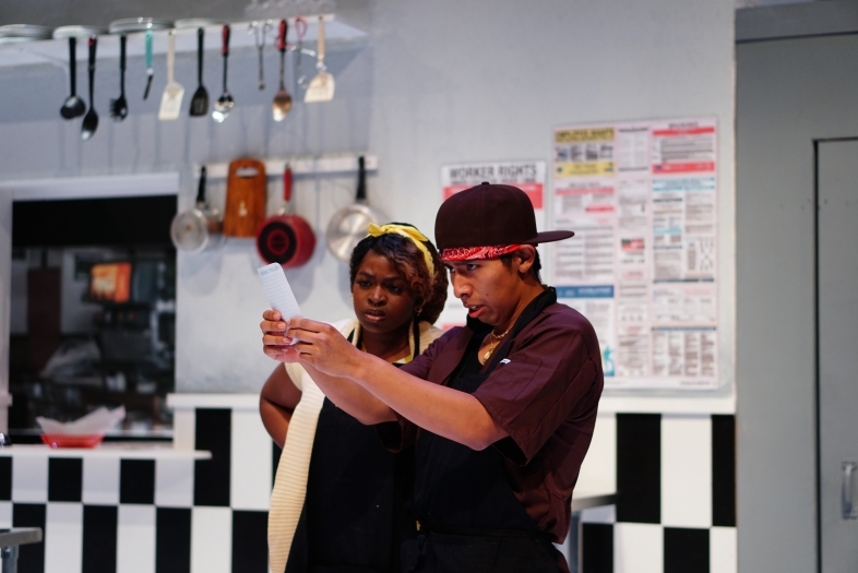 two young people stand in a kitchen holding a piece of paper