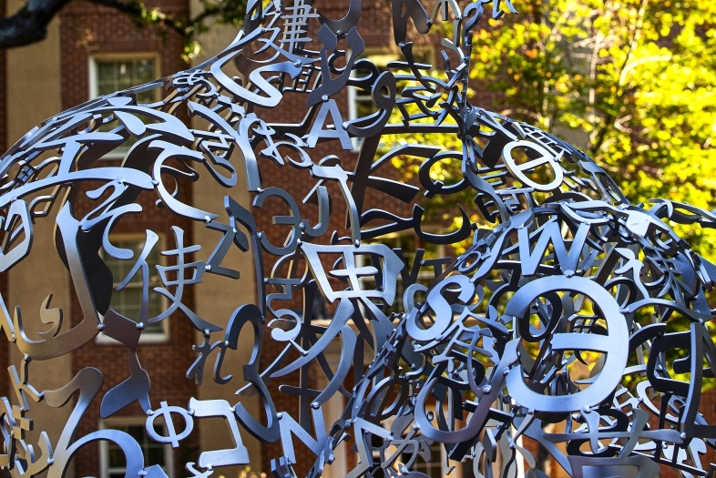 a silver sculpture made of metal letters with yellow and green foliage in the background