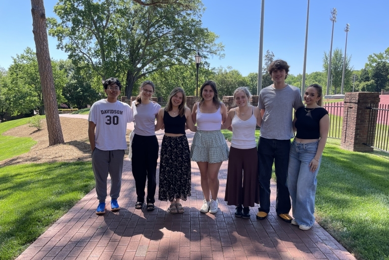 a group of young men and women standing together and smiling on a brick pathway