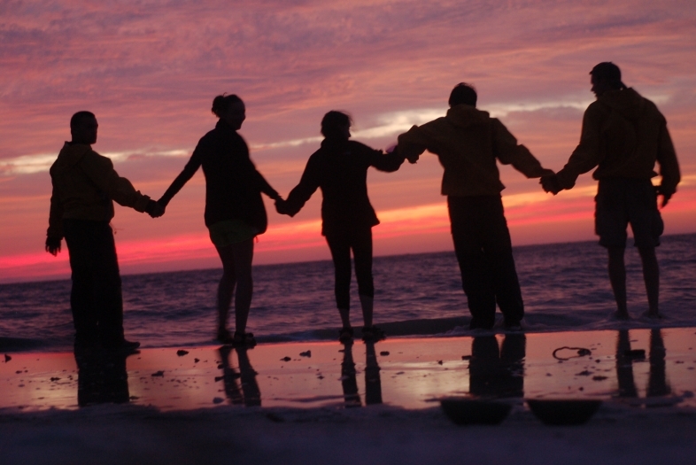 students on a beach, at sunset, holding hands