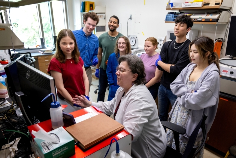 a group of students gather around a professor in a lab