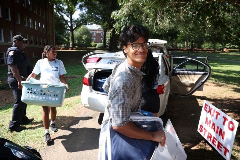 a young man moves into his dorm room while unpacking a car of stuff
