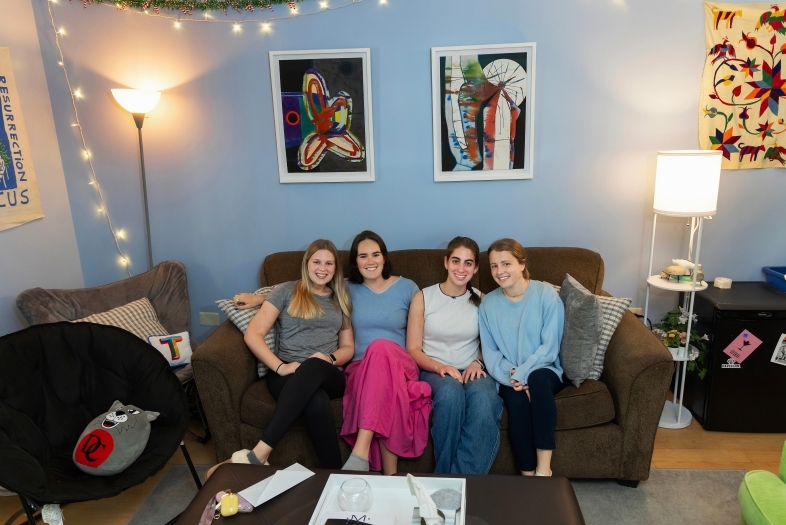 a group of four young women sit on a couch in an apartment