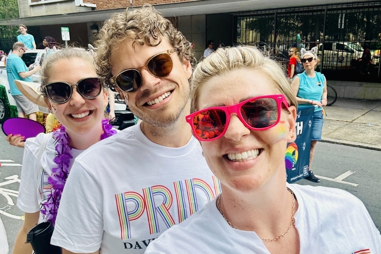 three young people smile together wearing "Davidson College Pride" shirts on a city street