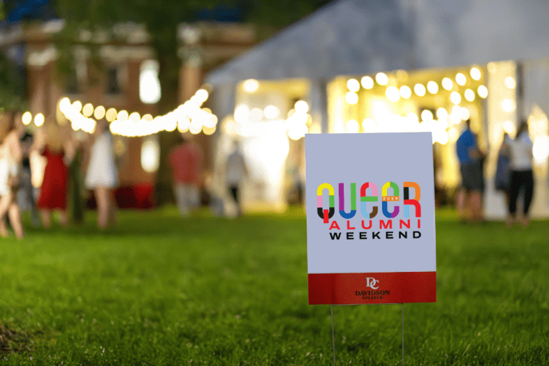 a lawn sign that reads "Queer Alumni Weekend" in front of a large white tent with string lights at night