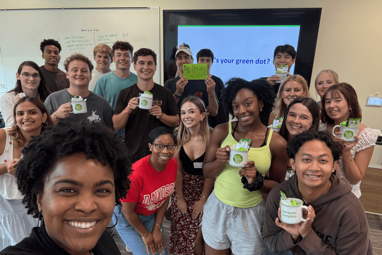 a group of students smile while holding mugs that read "Green Dot"