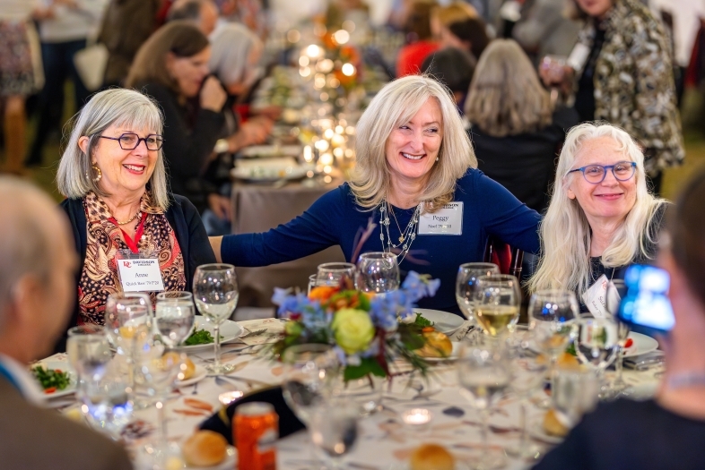 Three women with bright platinum hair sit at a dining table