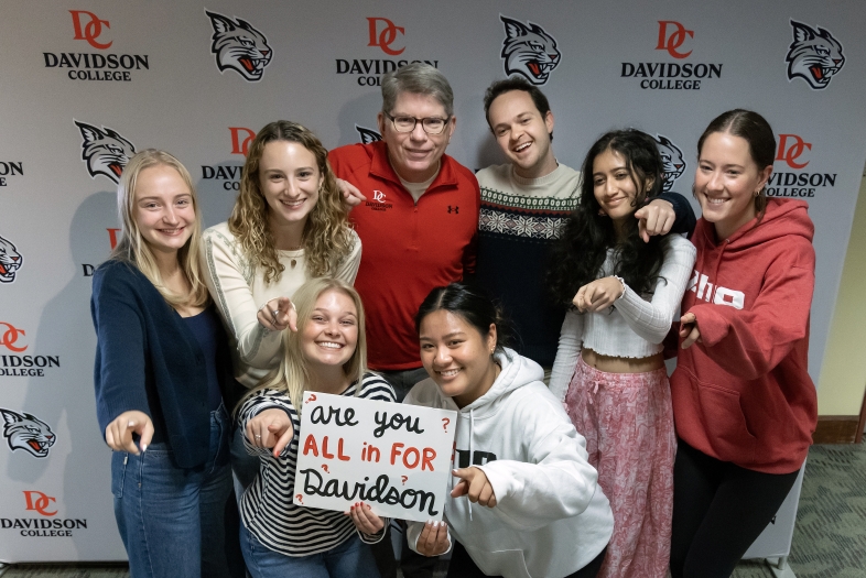 Group of students with Douglas Hicks in front of a branded Davidson banner