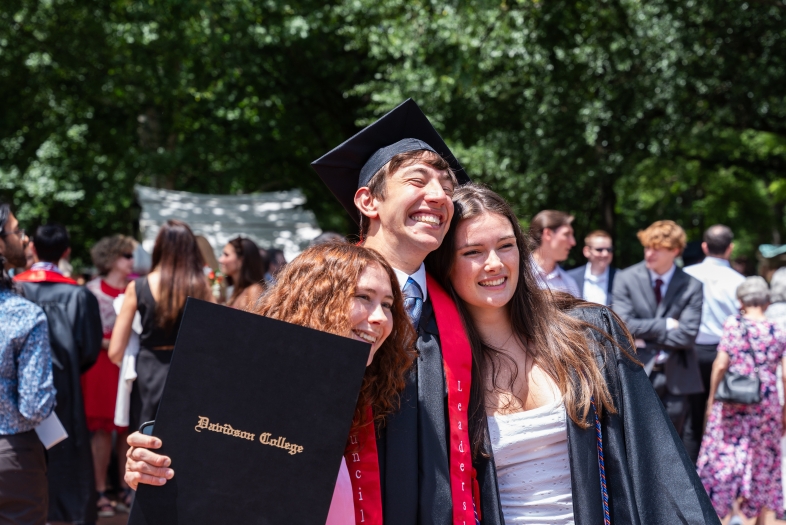 Commencement Three students hugging while getting photo taken, one student is holding his diploma