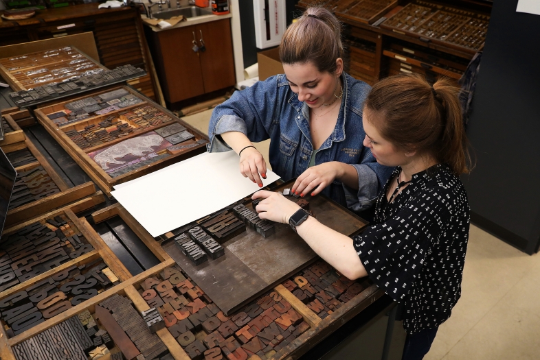 Two students or employees sort through letterpress equipment in the lab