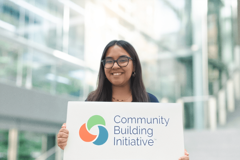 a young woman holds a sign that says "community building initiative"