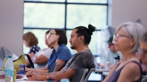 a group of adults in a classroom listening to a presentation