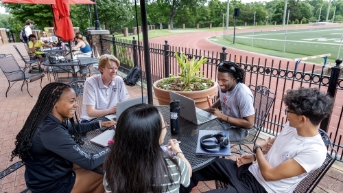 a group of students work on laptops at a table on a patio