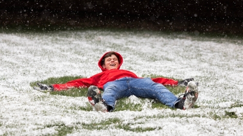 a young man makes a snow angel during winter time on college campus