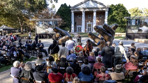 Seated crowd in front of With These Hands sculpture