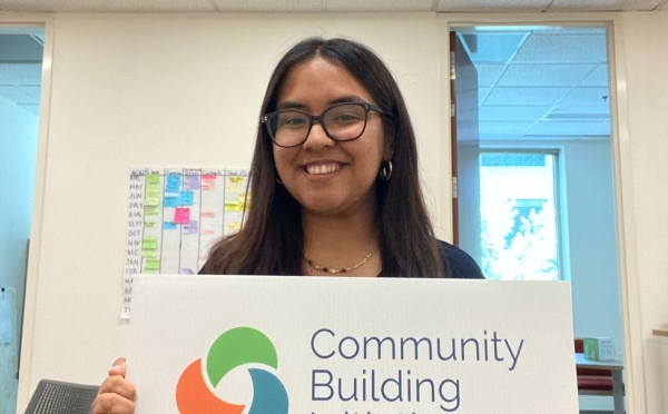 a young woman holds a sign that says "community building initiative"
