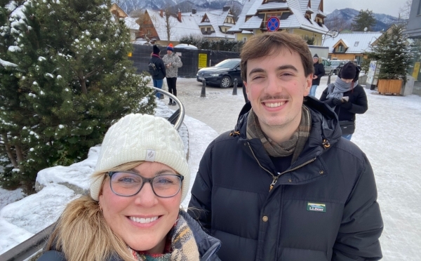 an older white woman and a younger white man smile in front of a snowy landscape
