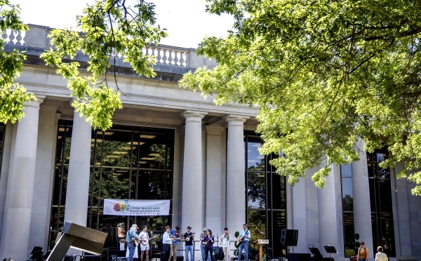 a group of students perform music in front of a columned academic building on a sunny day