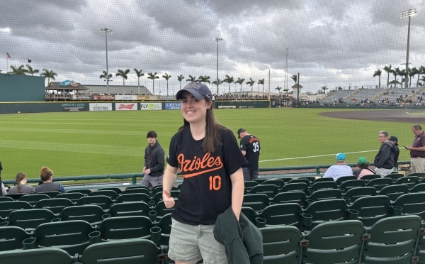 a young woman wearing an Orioles baseball jersey and hat in front of a baseball stadium