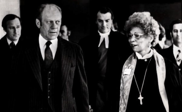 a Black woman walks and talks with an older white man in a black and white photograph