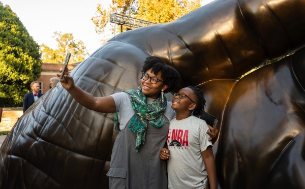 two young people smile and take a selfie in front of a sculpture