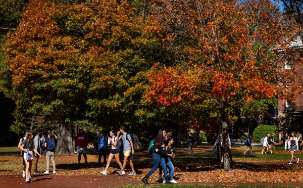 Students wearing backpacks walk past bright autumn foliage on the chambers lawn