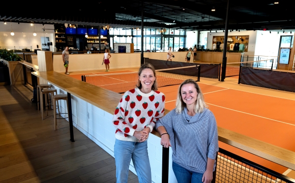 two women stand in front of an indoor pickleball space