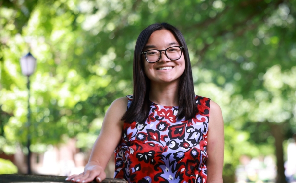 A smiling student with glasses and straight, dark hair poses outside wearing a sleeveless floral patterned blouse.