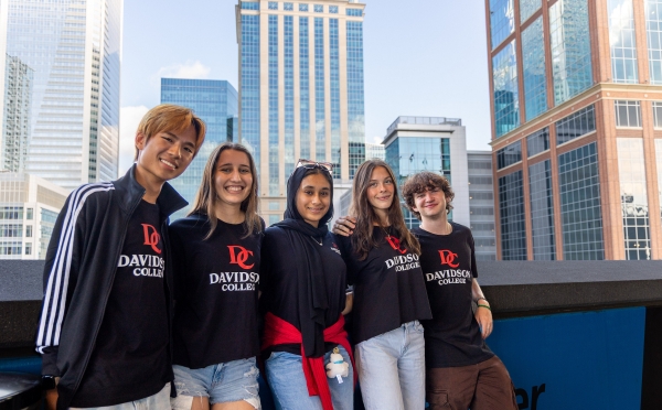 Five students in black and red Davidosn College shirts, with skyscrapers in the background