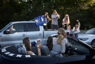 Friends in trunk of truck cheering with sign 