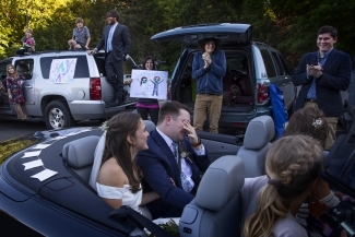 Caroline and Tyler smiling at guests in front of cars cheering