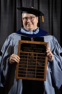 Melissa Gonzalez in cap and gown holds award plaque