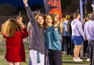 Two students smiling and waving at camera