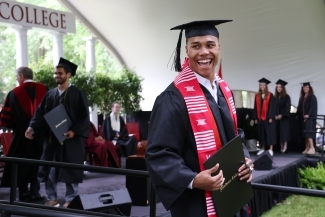 Student smiles at camera while holding diploma