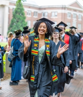 a young woman wears a graduation cap and gown and smiles