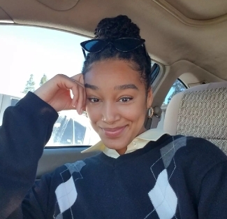 a young woman wearing a sweater and a bun with sunglasses on her head