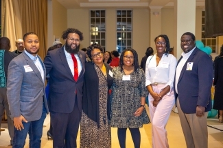 a group of Black men and women standing together smiling in dressy clothes
