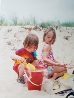 two little girls play in sand at beach