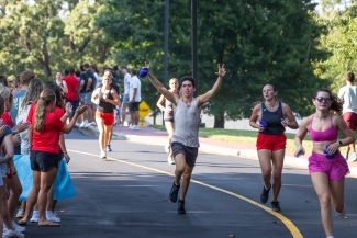 a young man raises his arms while running and smiling
