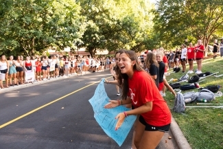 two young women clap and hold a sign along a road race