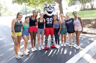 a group of young women in running clothes pose with Wildcat mascot